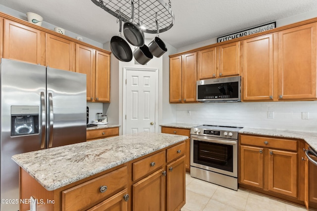 kitchen with stainless steel appliances, brown cabinets, light stone counters, and tasteful backsplash