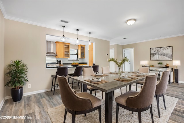 dining room featuring crown molding, light wood-type flooring, visible vents, and baseboards