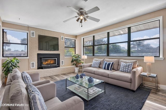 living room with a brick fireplace, ceiling fan, and wood finished floors