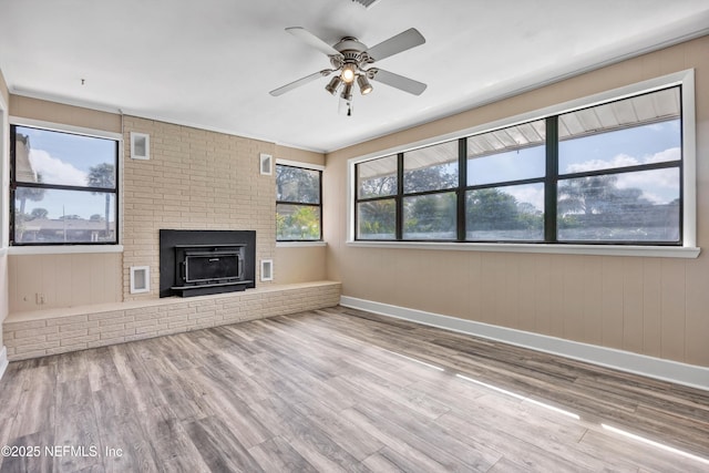 unfurnished living room featuring ceiling fan, a fireplace, baseboards, and wood finished floors