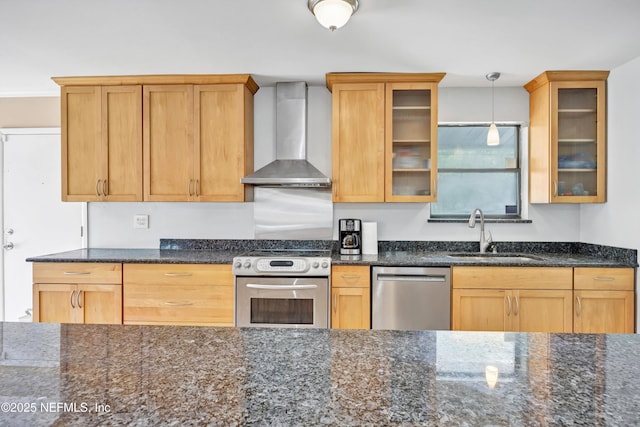 kitchen with stainless steel appliances, a sink, wall chimney exhaust hood, glass insert cabinets, and pendant lighting