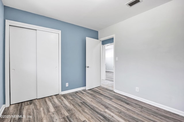 unfurnished bedroom with baseboards, a closet, visible vents, and wood finished floors