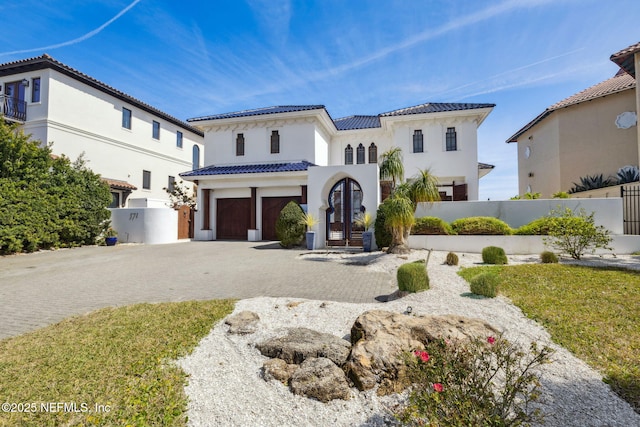 mediterranean / spanish house featuring decorative driveway, an attached garage, and fence