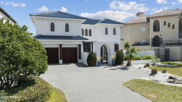 mediterranean / spanish house featuring a garage, a tile roof, fence, decorative driveway, and stucco siding