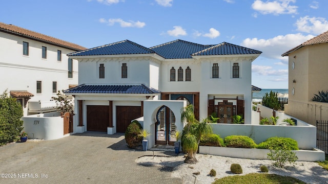 mediterranean / spanish-style house with a fenced front yard, decorative driveway, a tile roof, and an attached garage