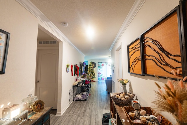 corridor with a textured ceiling, ornamental molding, visible vents, and light wood-style floors