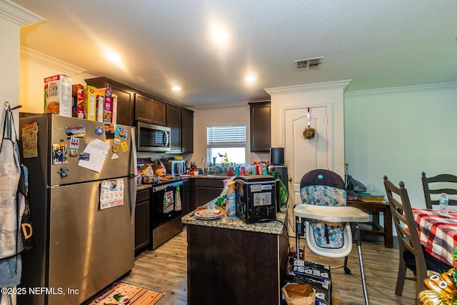 kitchen with stainless steel appliances, visible vents, dark brown cabinets, ornamental molding, and light wood finished floors