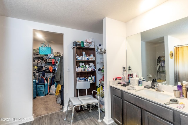 bathroom featuring wood finished floors, a walk in closet, a textured ceiling, and vanity