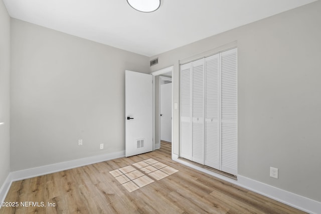 unfurnished bedroom featuring baseboards, a closet, visible vents, and wood finished floors