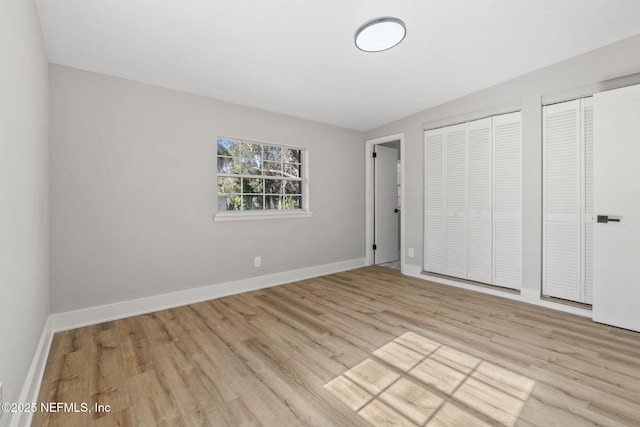 unfurnished bedroom featuring baseboards, wood finished floors, and multiple closets