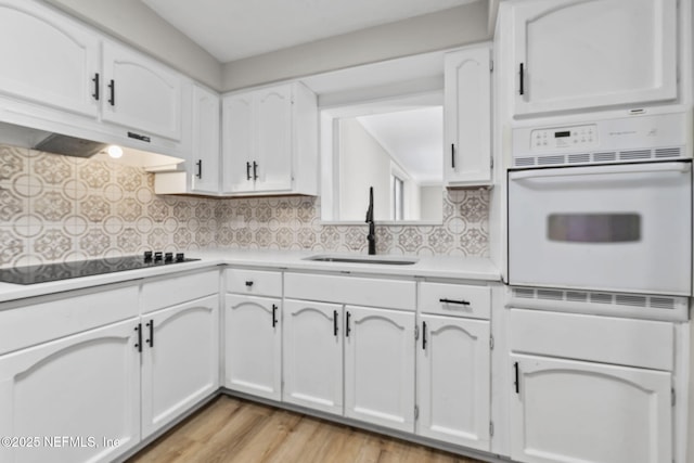 kitchen featuring white oven, black electric stovetop, decorative backsplash, white cabinetry, and a sink