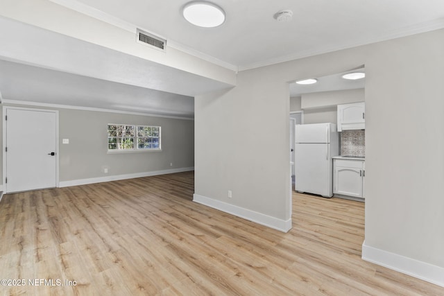 spare room featuring light wood finished floors, visible vents, baseboards, and crown molding