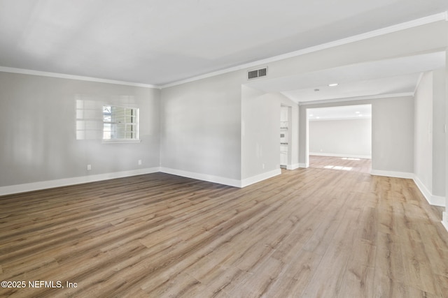 spare room with baseboards, wood finished floors, visible vents, and crown molding