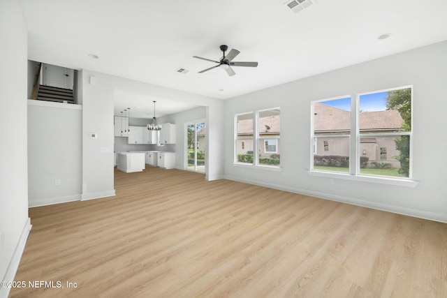 unfurnished living room featuring light wood-style floors, baseboards, visible vents, and ceiling fan with notable chandelier