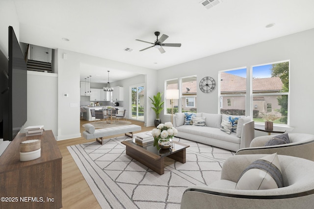 living area featuring light wood-style floors, visible vents, baseboards, and ceiling fan with notable chandelier