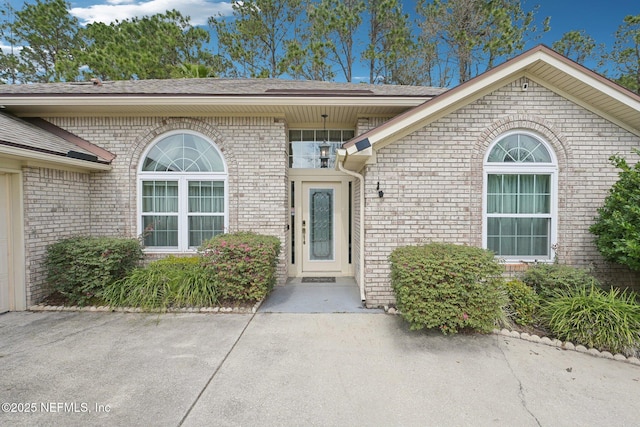 property entrance with a shingled roof and brick siding