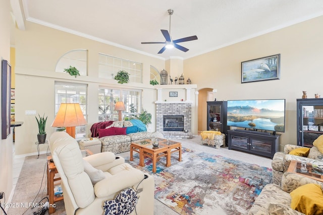 carpeted living room featuring ceiling fan, ornamental molding, a brick fireplace, and arched walkways