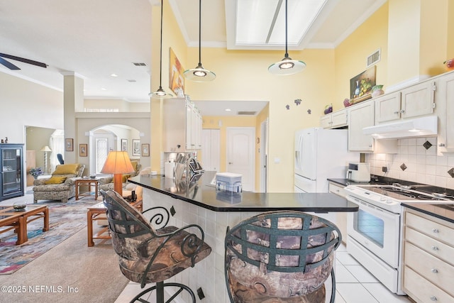 kitchen with white appliances, visible vents, dark countertops, a kitchen breakfast bar, and under cabinet range hood