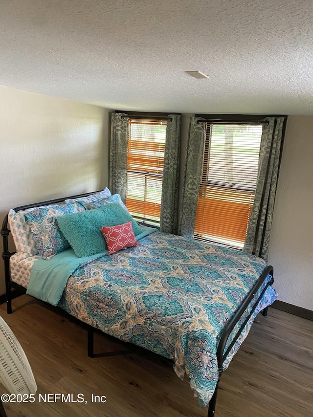 bedroom with a textured ceiling, wood finished floors, and baseboards