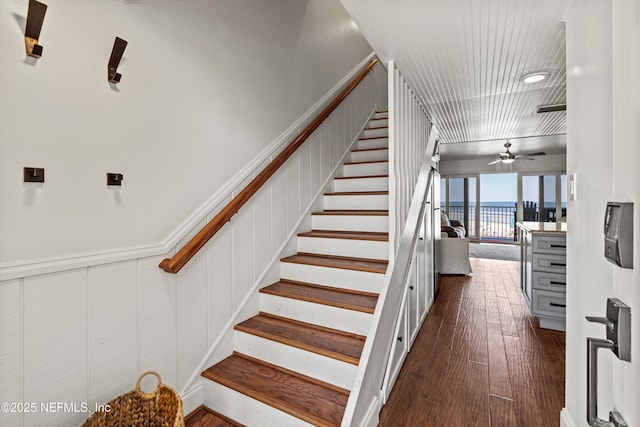 staircase featuring a wainscoted wall, a decorative wall, ceiling fan, and wood finished floors