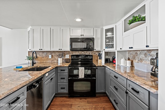 kitchen with light stone countertops, dark wood finished floors, gray cabinets, a sink, and black appliances