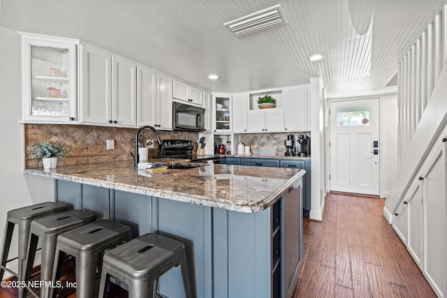 kitchen featuring visible vents, black appliances, glass insert cabinets, a peninsula, and white cabinetry