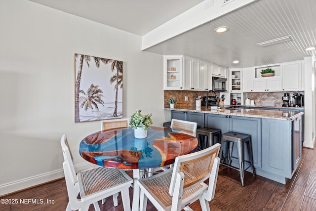 dining space featuring dark wood finished floors, beam ceiling, and baseboards