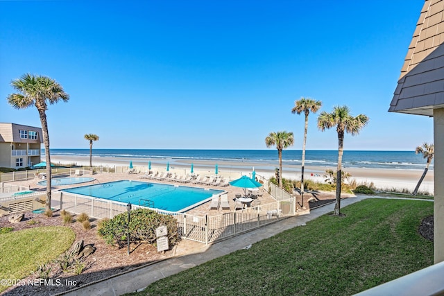 community pool with a patio, a lawn, a water view, and fence