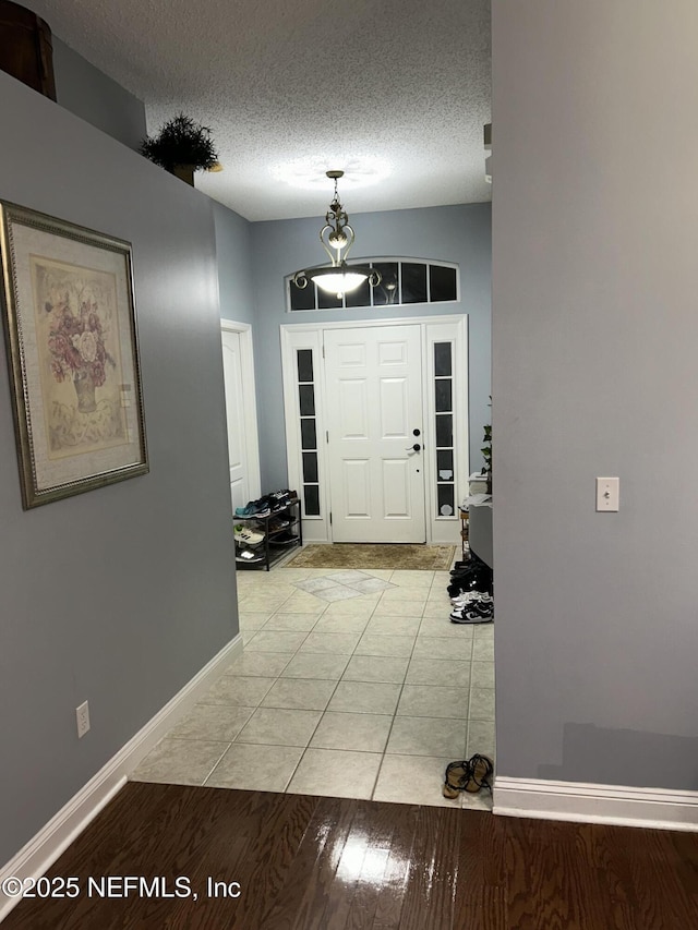 foyer entrance featuring a textured ceiling, light tile patterned floors, and baseboards