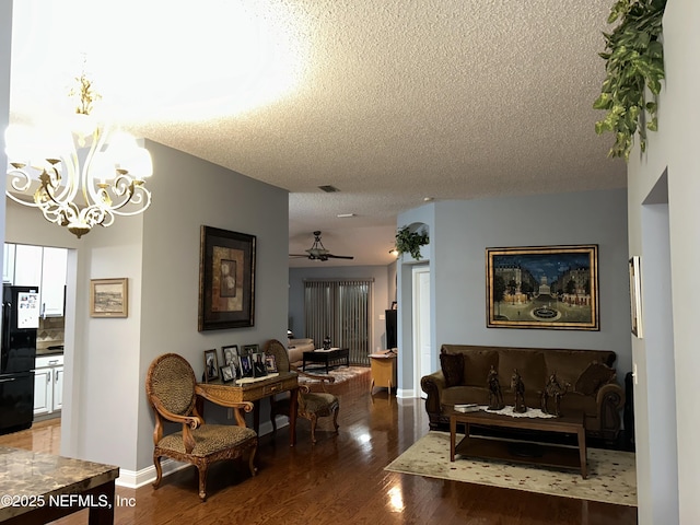 living room featuring baseboards, visible vents, wood finished floors, a textured ceiling, and ceiling fan with notable chandelier