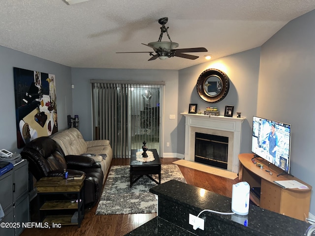 living room with baseboards, a fireplace with flush hearth, ceiling fan, wood finished floors, and a textured ceiling