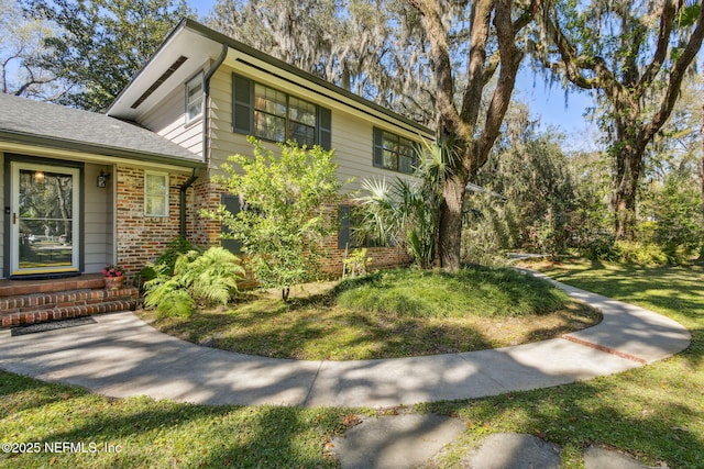 view of front facade with a front yard, brick siding, and a shingled roof