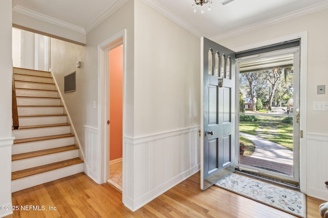 foyer entrance with wainscoting, stairs, light wood-style floors, and ornamental molding