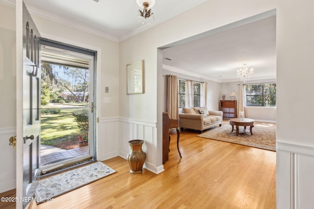 entrance foyer featuring a notable chandelier, ornamental molding, a wainscoted wall, and wood finished floors