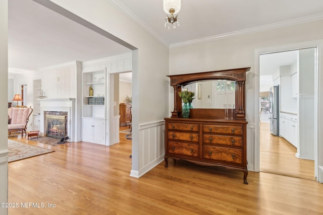 hall featuring built in features, light wood-style floors, a chandelier, and crown molding