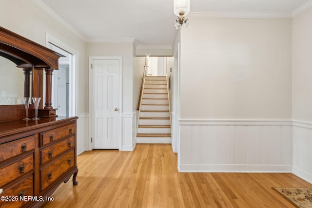 interior space with stairs, light wood-style flooring, a wainscoted wall, and ornamental molding