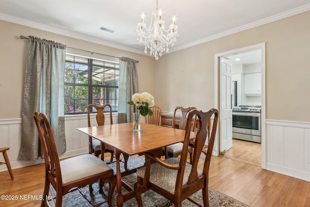 dining space featuring light wood finished floors, visible vents, a chandelier, a wainscoted wall, and ornamental molding