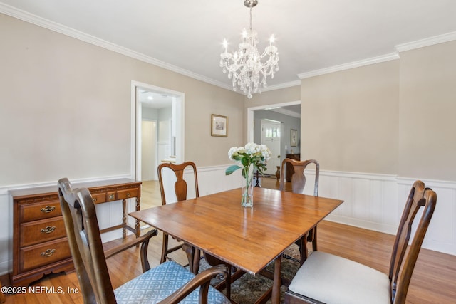 dining area featuring wainscoting, a notable chandelier, light wood-style flooring, and crown molding