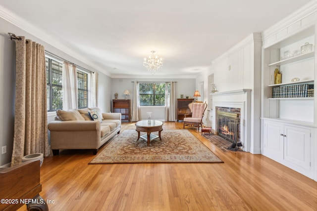 living area featuring built in shelves, a fireplace with flush hearth, light wood-style flooring, and ornamental molding