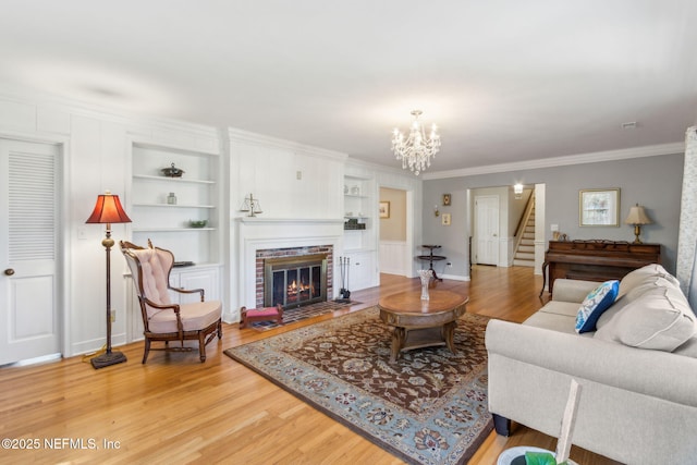 living room featuring built in shelves, a fireplace, stairs, light wood-style floors, and a chandelier