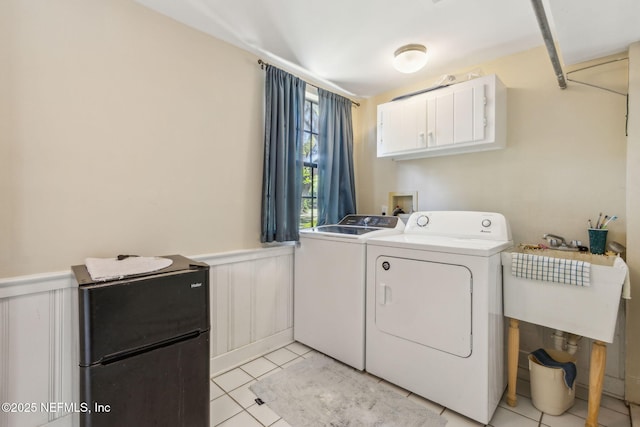 washroom featuring light tile patterned floors, cabinet space, a sink, wainscoting, and washer and clothes dryer