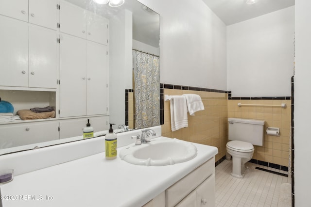 bathroom featuring tile patterned flooring, tile walls, a wainscoted wall, toilet, and vanity