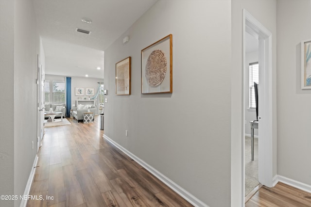 hallway featuring wood finished floors, visible vents, and baseboards