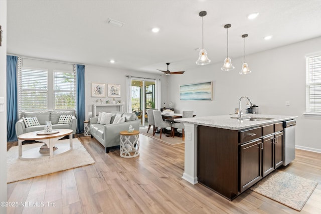 kitchen with a sink, light wood-style floors, open floor plan, dark brown cabinets, and stainless steel dishwasher