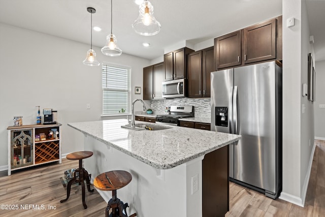 kitchen featuring decorative backsplash, appliances with stainless steel finishes, a breakfast bar area, dark brown cabinets, and a sink