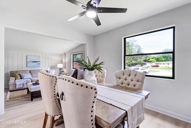 dining space with a ceiling fan, baseboards, vaulted ceiling, and light wood finished floors