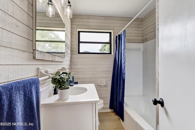 full bath with toilet, wood walls, shower / bath combo with shower curtain, and vanity