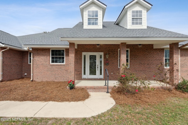 view of front of home with roof with shingles, a porch, and brick siding