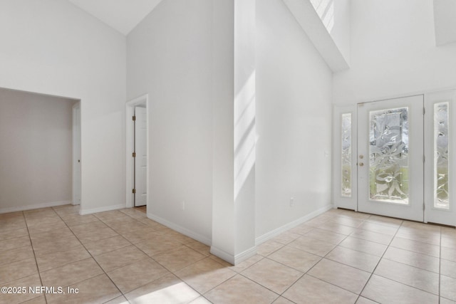 foyer entrance with light tile patterned floors, baseboards, and high vaulted ceiling