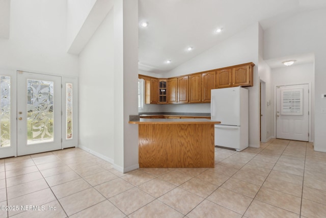 kitchen with light tile patterned floors, glass insert cabinets, brown cabinets, freestanding refrigerator, and a peninsula